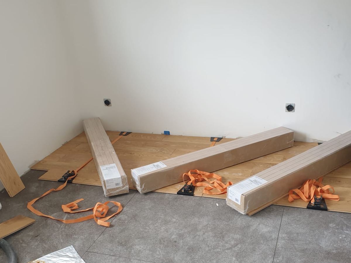 Pose collée de parquet en bois massif en cours, lames sanglées en attente de prise de la colle